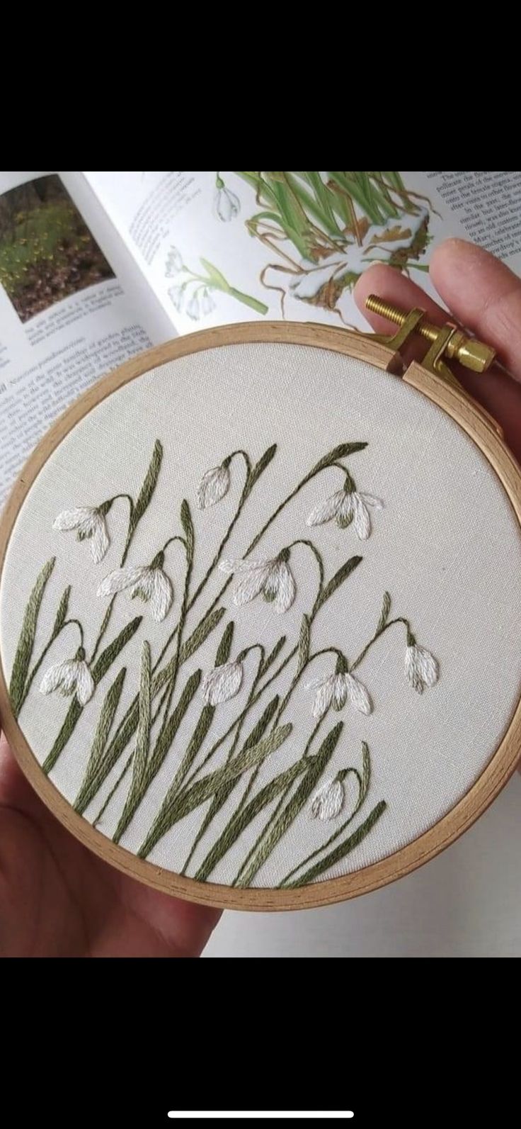 a hand holding a cross stitched white and green floral design on a book page