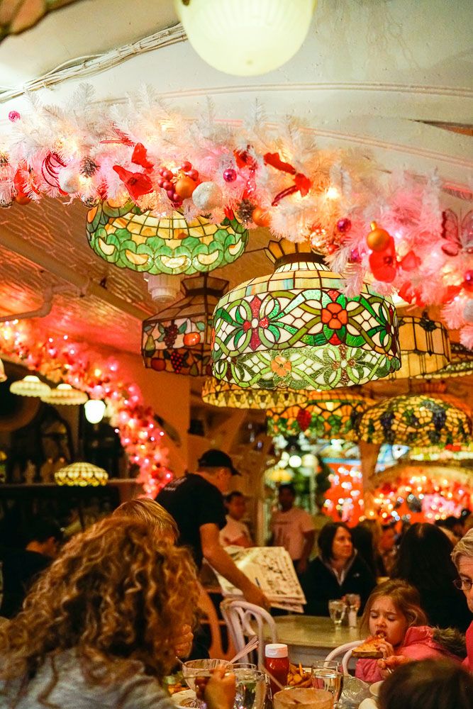 people sitting at tables in a restaurant with colorful lights hanging from the ceiling above them