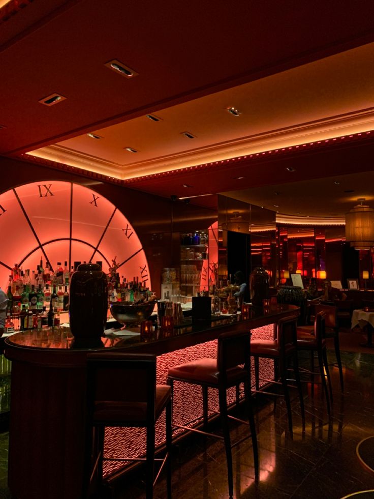 a dimly lit bar with stools and tables in front of the bar area at night