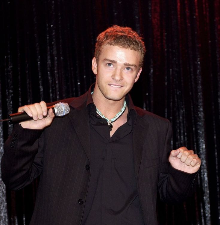 a man holding a microphone in his right hand while standing next to a stage curtain