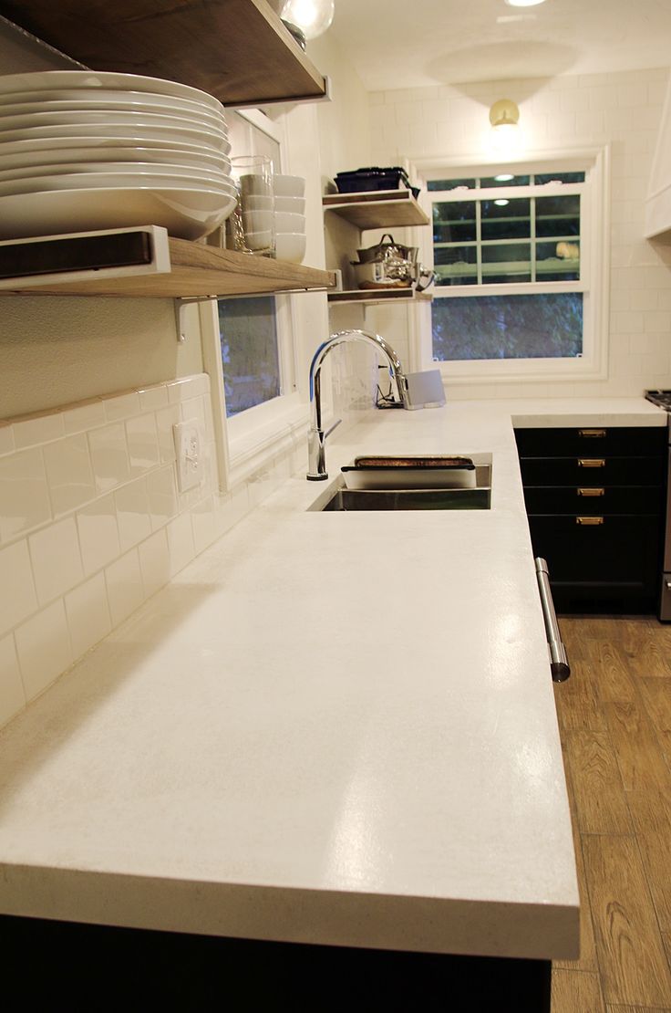 a white counter top in a kitchen next to a stove and sink with dishes on the shelves