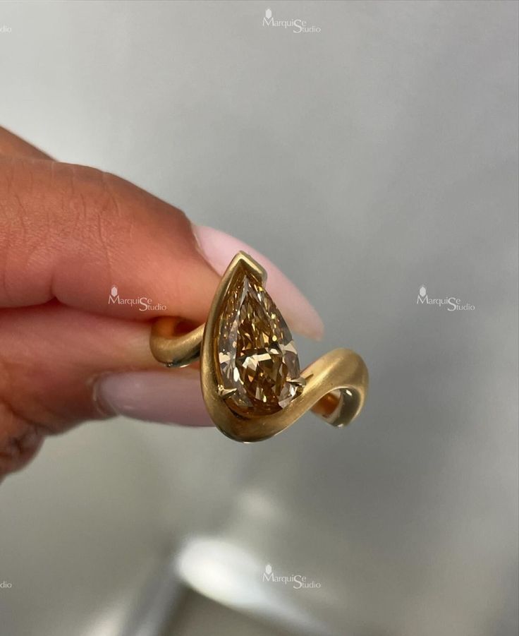 a woman's hand holding a gold ring with a brown diamond in the middle