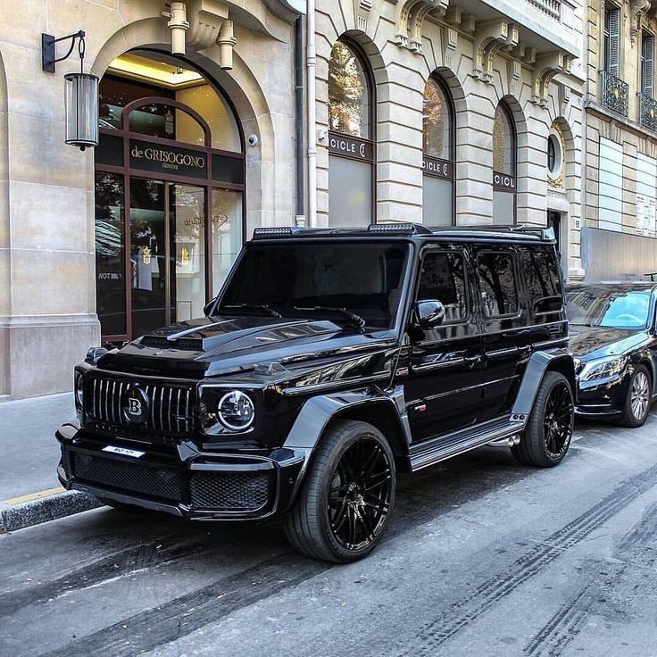 a black mercedes g - class parked in front of a building on a city street