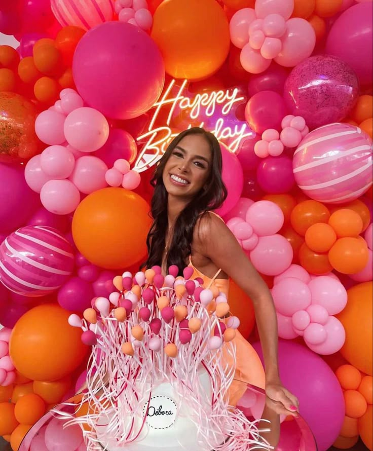 a woman standing in front of a cake with candles on it and balloons all around her