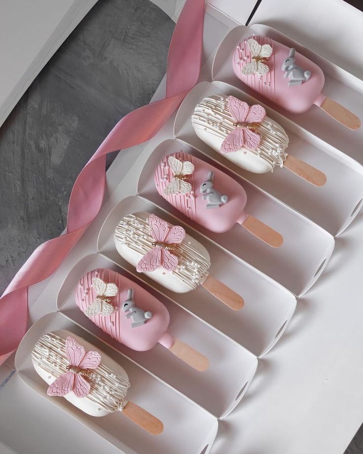 six cupcakes in pink and white decorated like hearts with bows on them sitting in a box