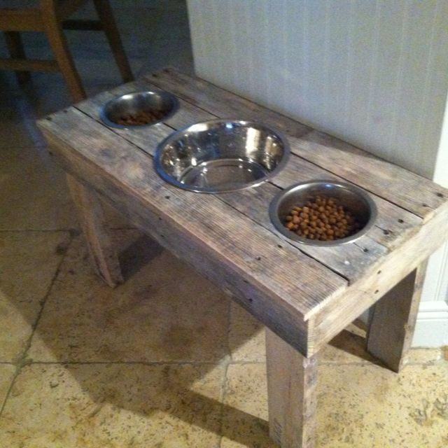 a wooden table with two metal bowls on it and one dog bowl in the middle