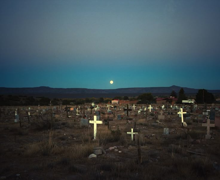 a cemetery with crosses in the foreground and a full moon in the sky above