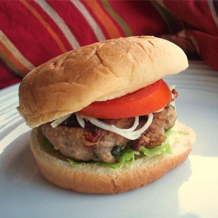 a sandwich with meat, tomato and onions on a bun sitting on a white plate