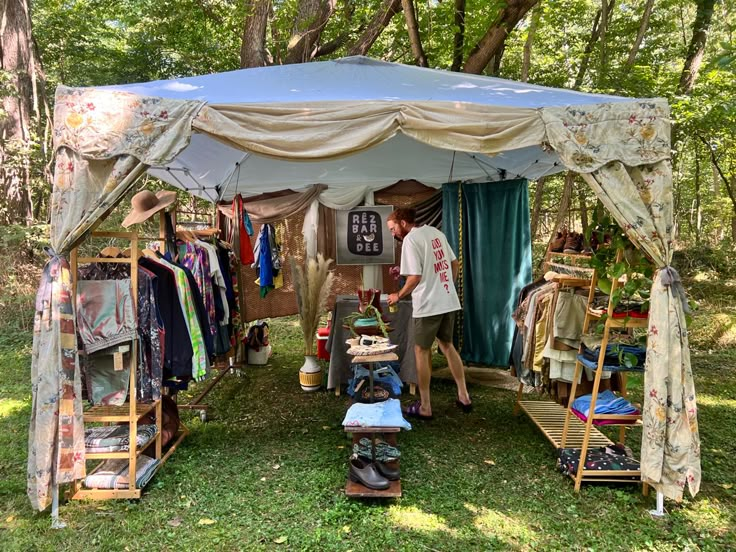 two people standing in front of a tent with clothing on it and clothes hanging up