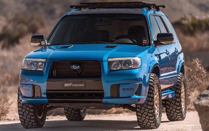 the front end of a blue suv driving down a dirt road