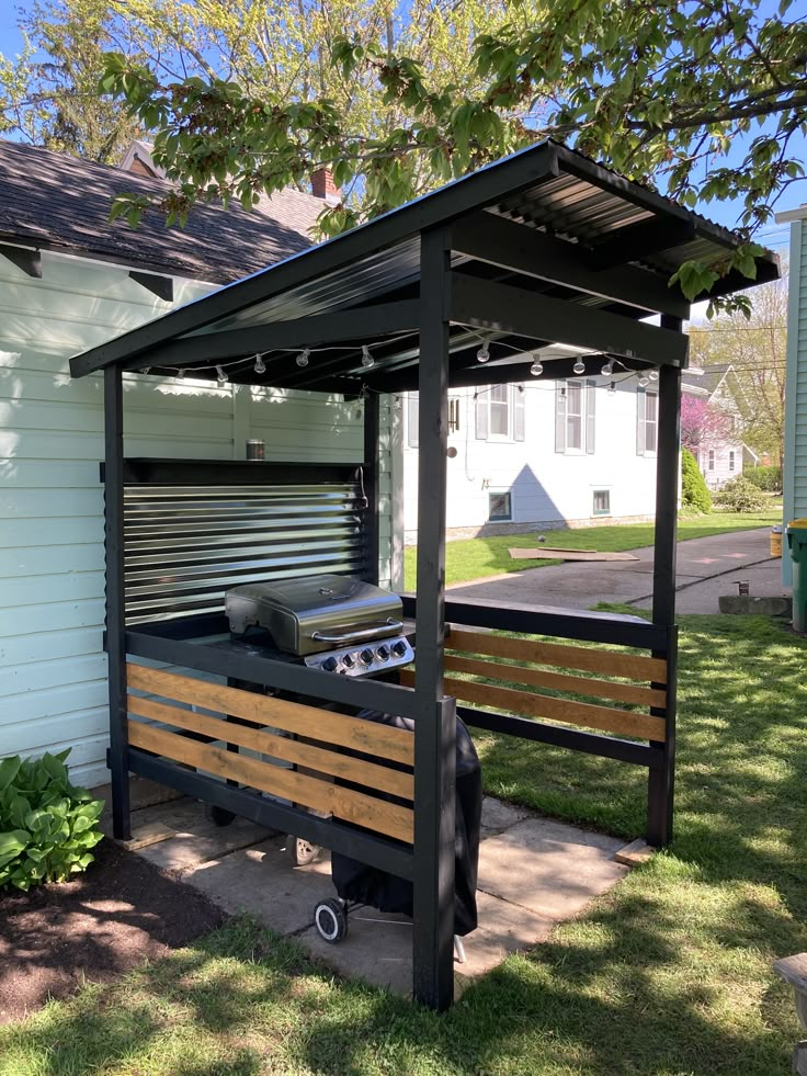 a wooden bench sitting in the grass under a canopy next to a white house and trees