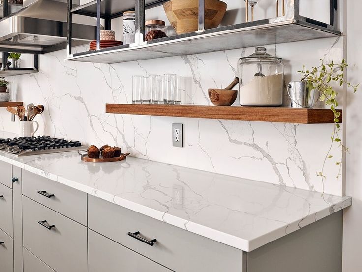 a kitchen with white marble counter tops and stainless steel shelving above the stove top