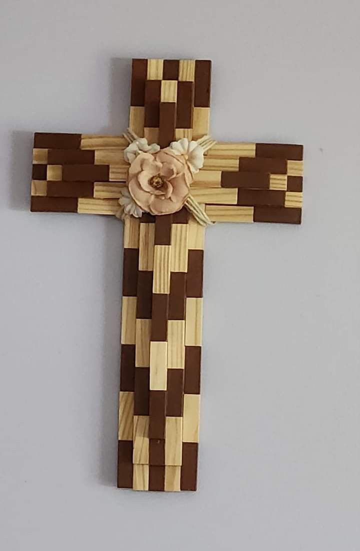 a wooden cross hanging on the wall with a flower decoration in it's center