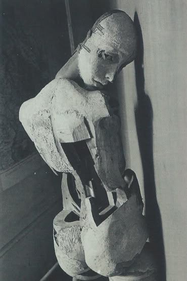 an old black and white photo of a man holding a bag in his hands, standing next to a wall