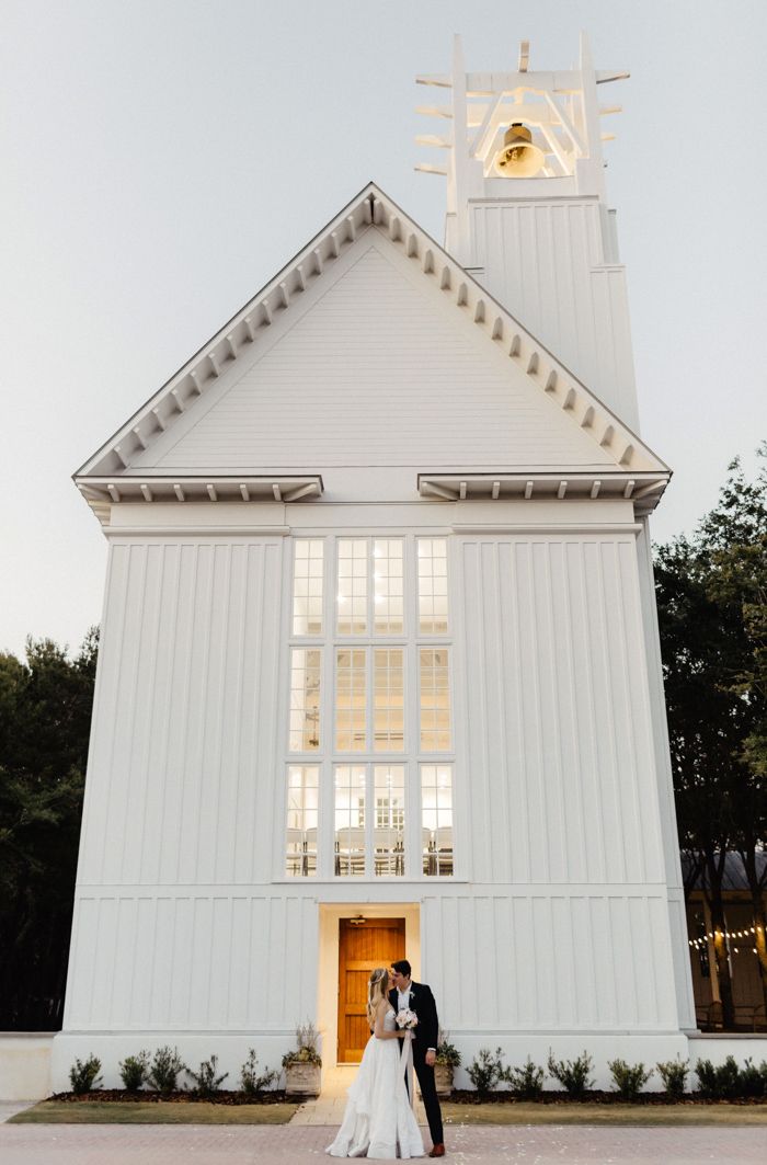 a bride and groom standing in front of a white church with the sun shining through the windows