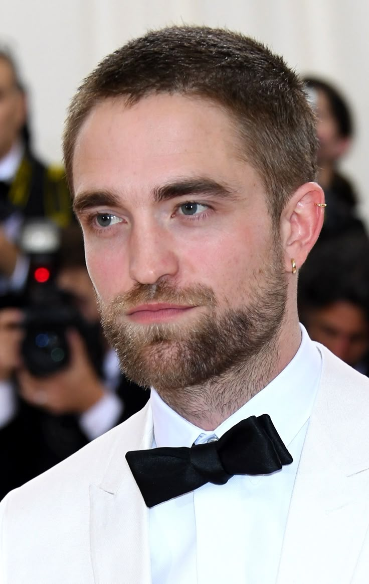 a man in a white suit and bow tie posing for the camera with cameras around him