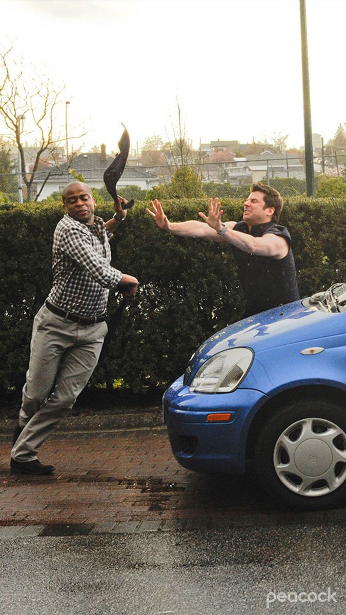 two men standing next to each other near a blue car