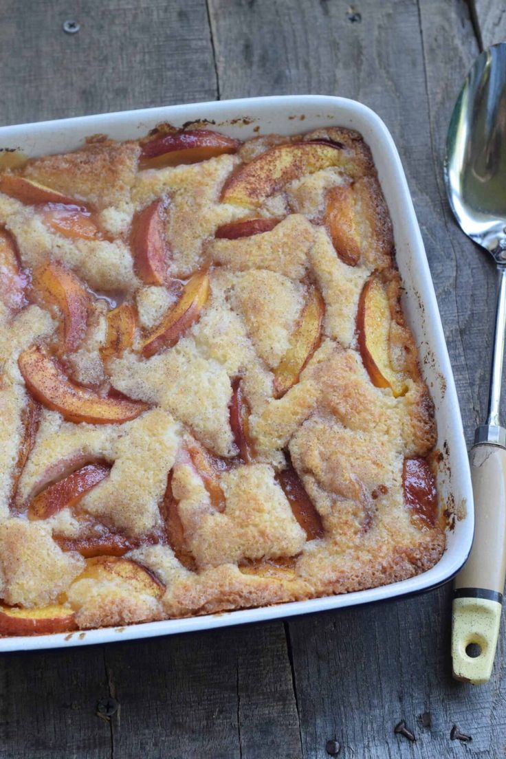 an apple cobbler in a white dish next to a fork and spoon on a wooden table