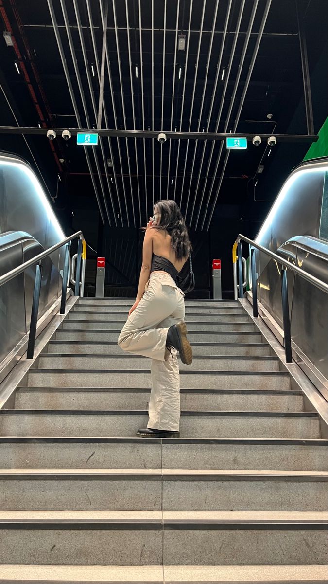 a woman is standing on the stairs in front of an escalator with her legs crossed