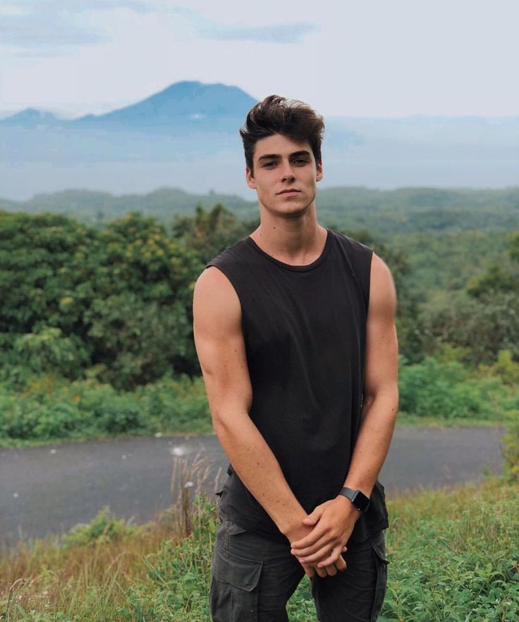 a young man standing on top of a lush green hillside