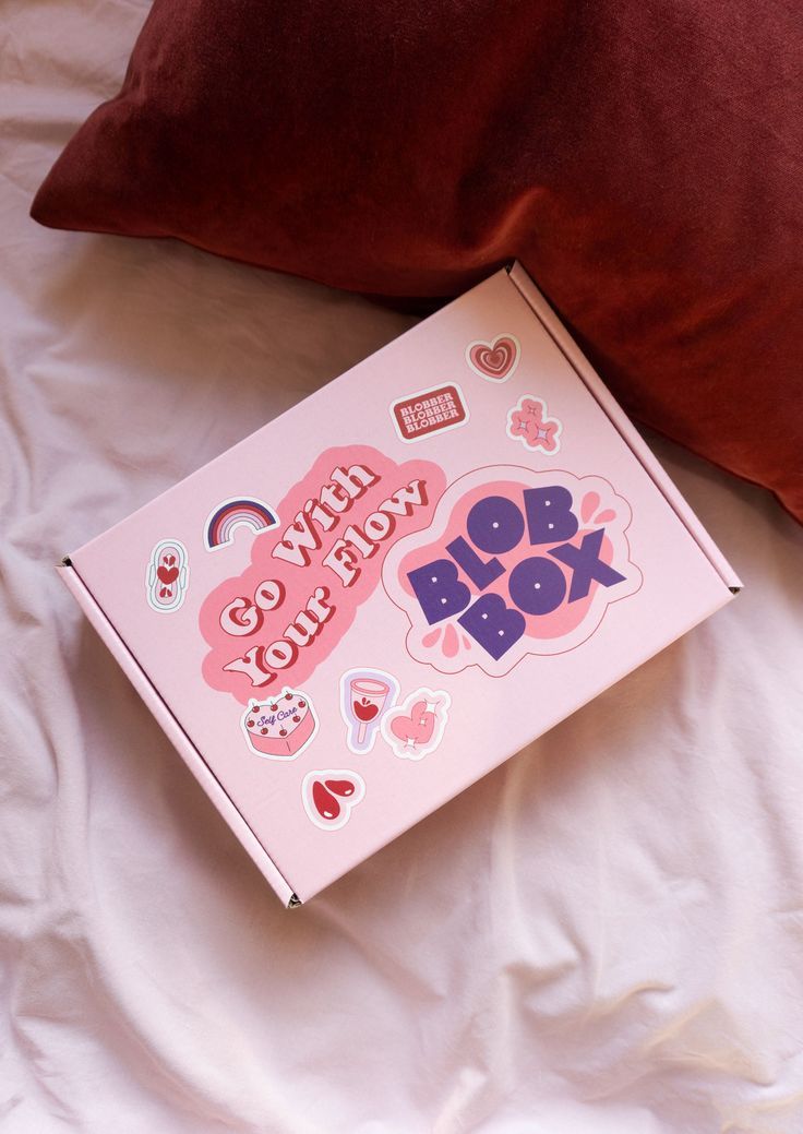 a pink box sitting on top of a bed next to a pillow