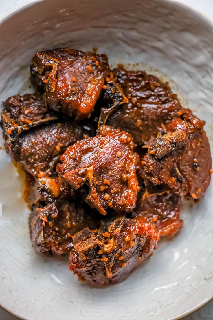 a white bowl filled with meat covered in sauce