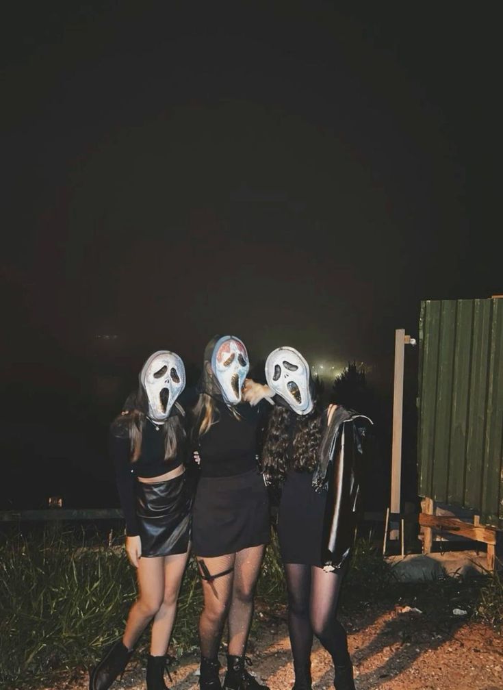 three girls with masks on their heads are standing in front of a fence at night