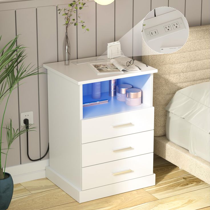 a white night stand with blue drawers and a plant on it next to a bed