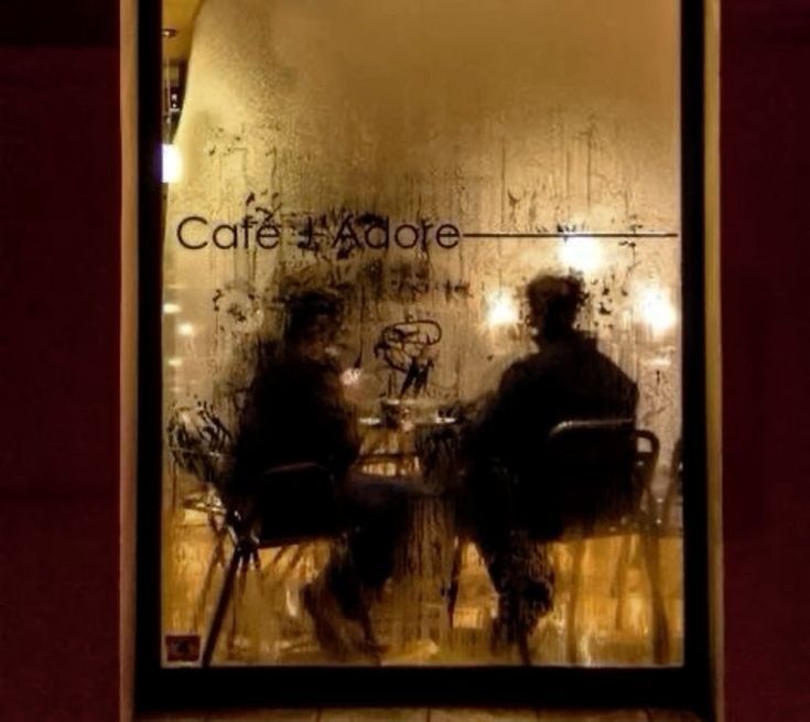 two people sitting at a table in front of a window with the words cafe adore written on it