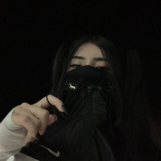 a woman wearing a black mask and holding something up to her face in the dark