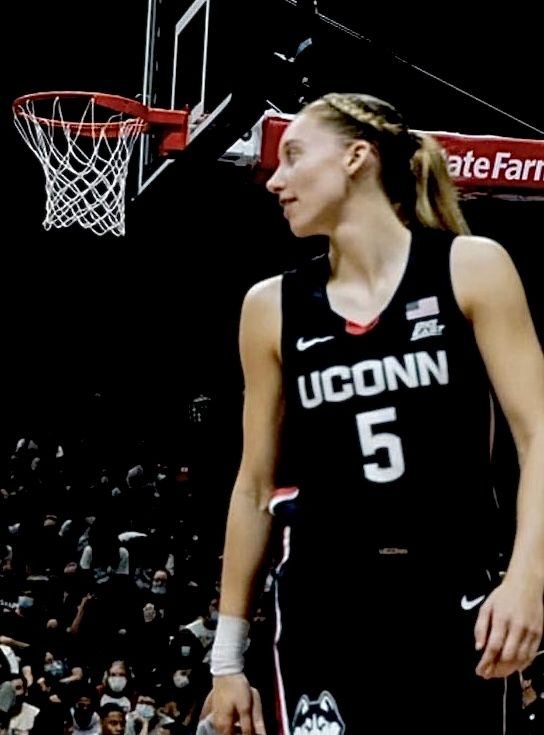 a woman standing in front of a basketball hoop with her hand on her hip and people watching from the bleachers