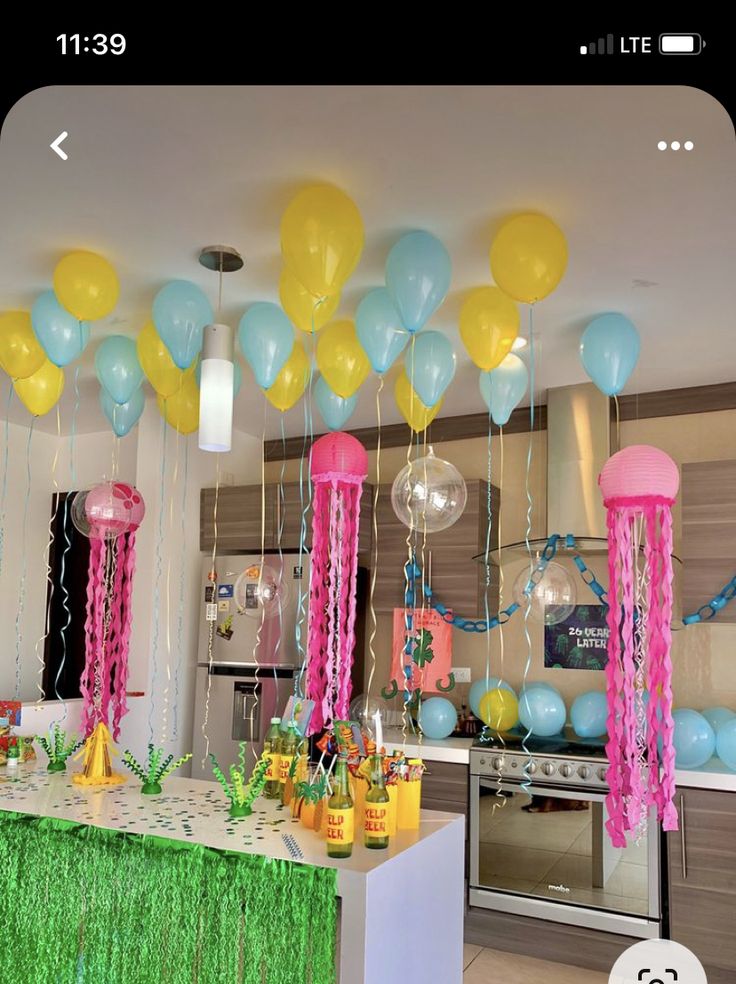 balloons and streamers are hanging from the ceiling in a kitchen area at a birthday party