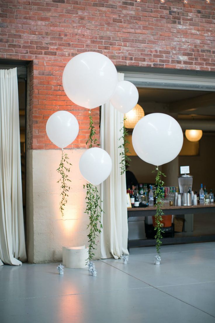 white balloons and greenery are hanging from the ceiling in front of a brick wall