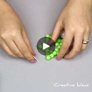 two hands are holding green beads and pointing them at each other's thumbnails