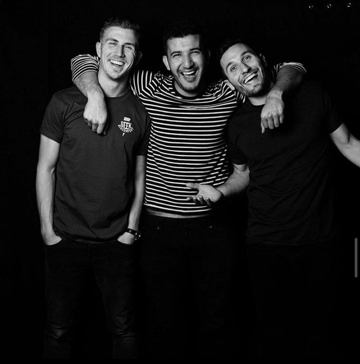 black and white photograph of three men laughing together, one is holding his arm around the other's shoulder