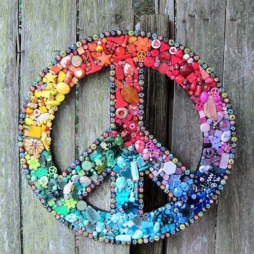 a peace sign made out of buttons and beads on a wooden surface with a fence in the background