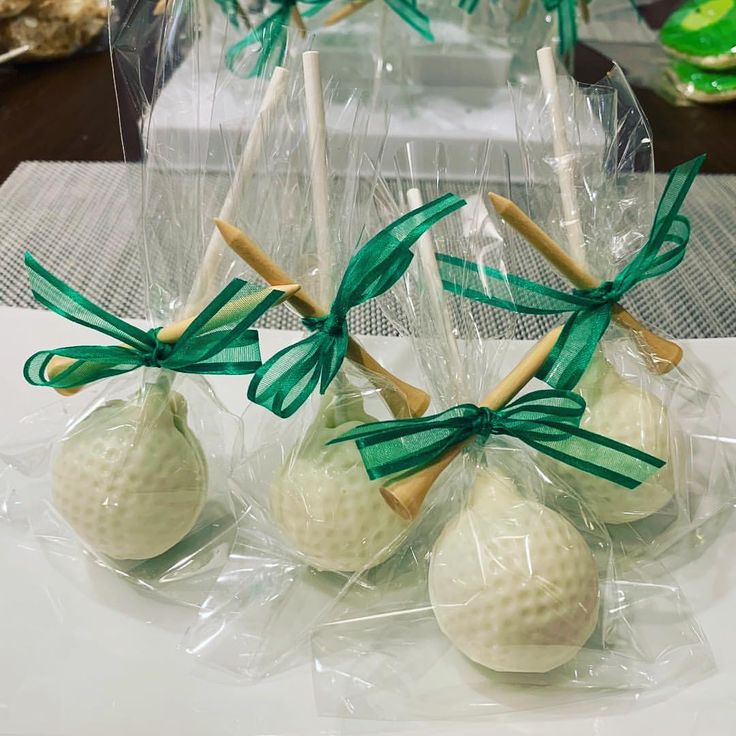 four golf balls wrapped in cellophane and tied with green ribbon, sitting on a table