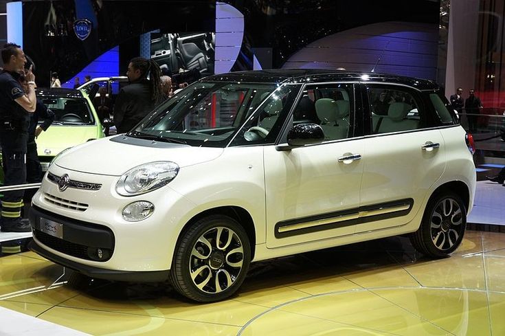 a small white car is on display at an auto show while people are taking pictures