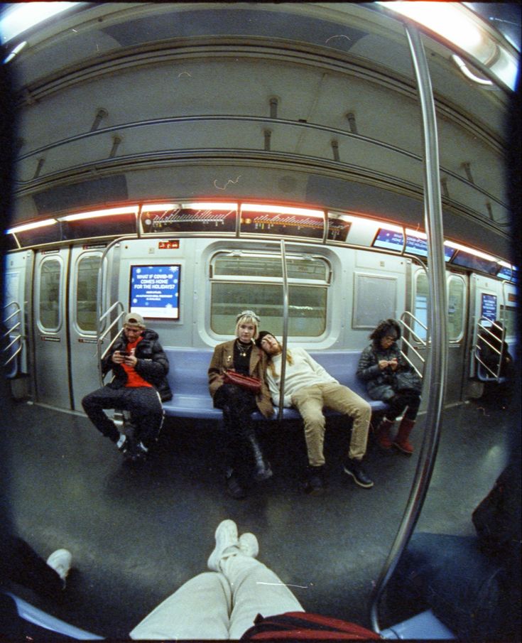 three people sitting on a subway car with their feet up in the air and one person taking a selfie