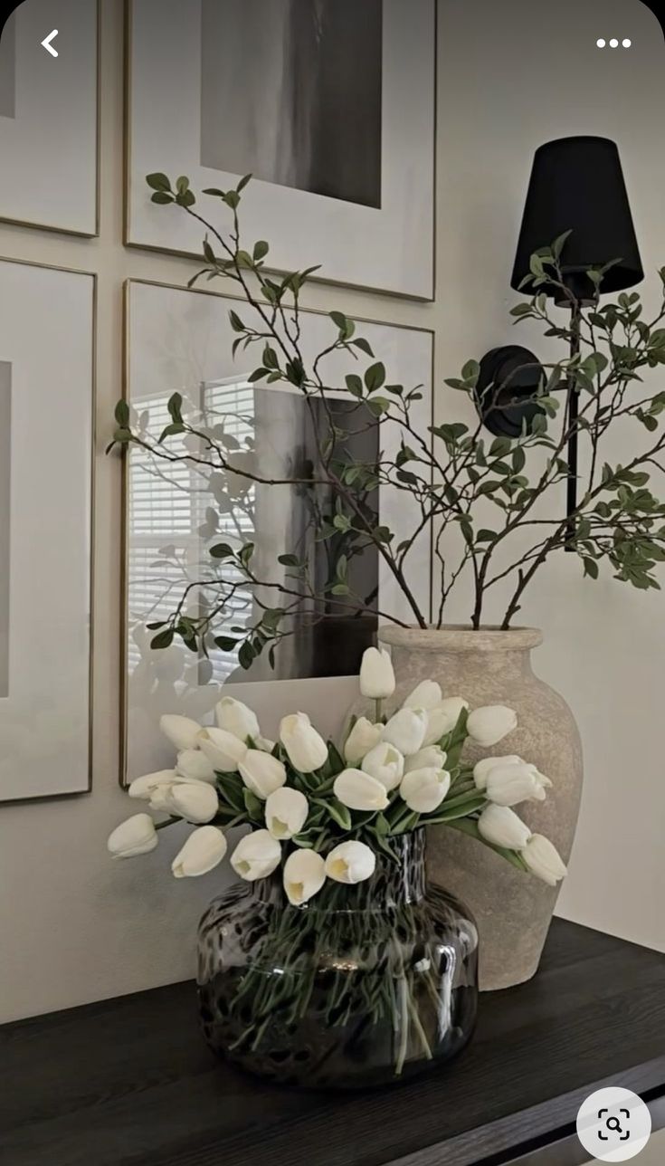 a vase filled with white flowers sitting on top of a table next to framed pictures