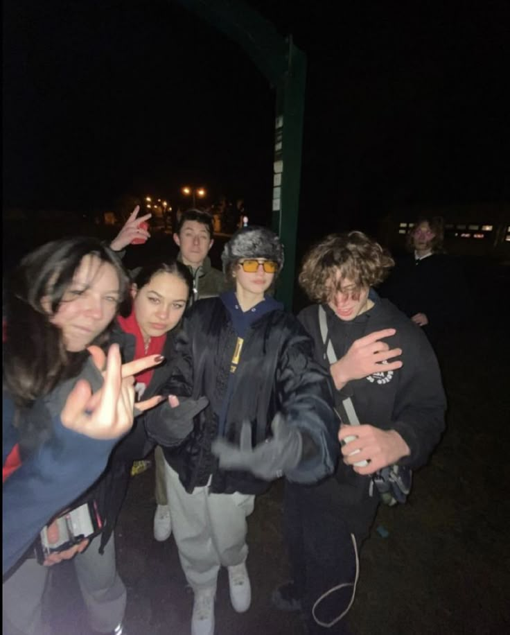 a group of people standing next to each other on a street at night with their hands in the air