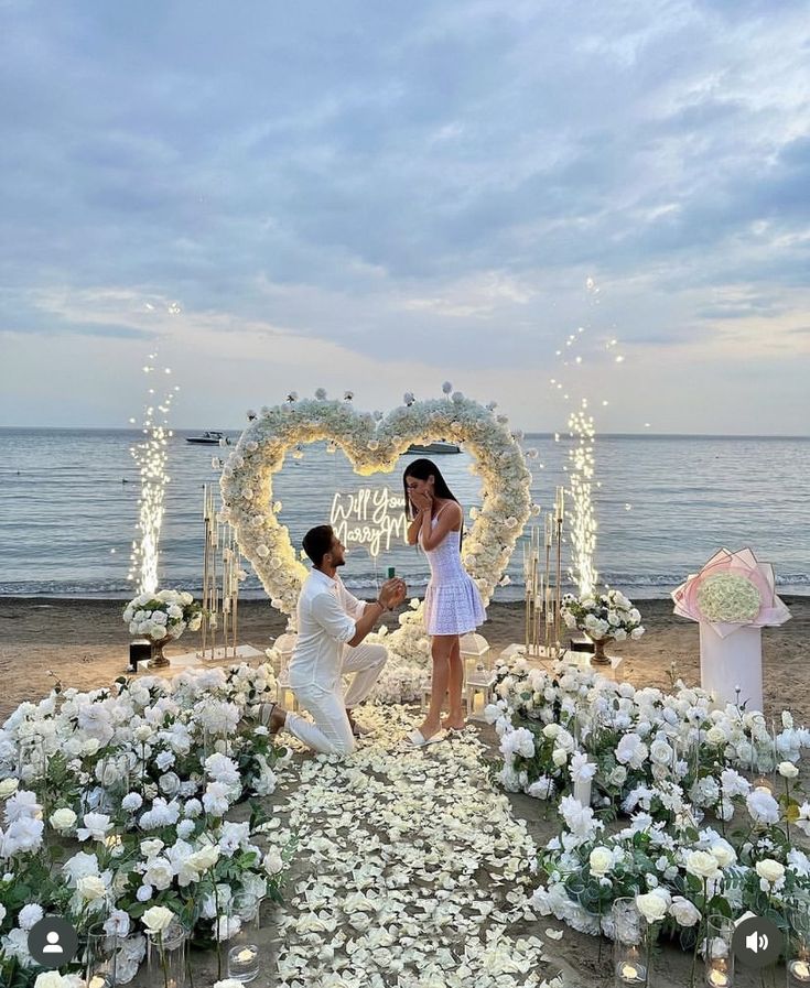 a newly married couple standing in front of a heart - shaped arch with flowers on it