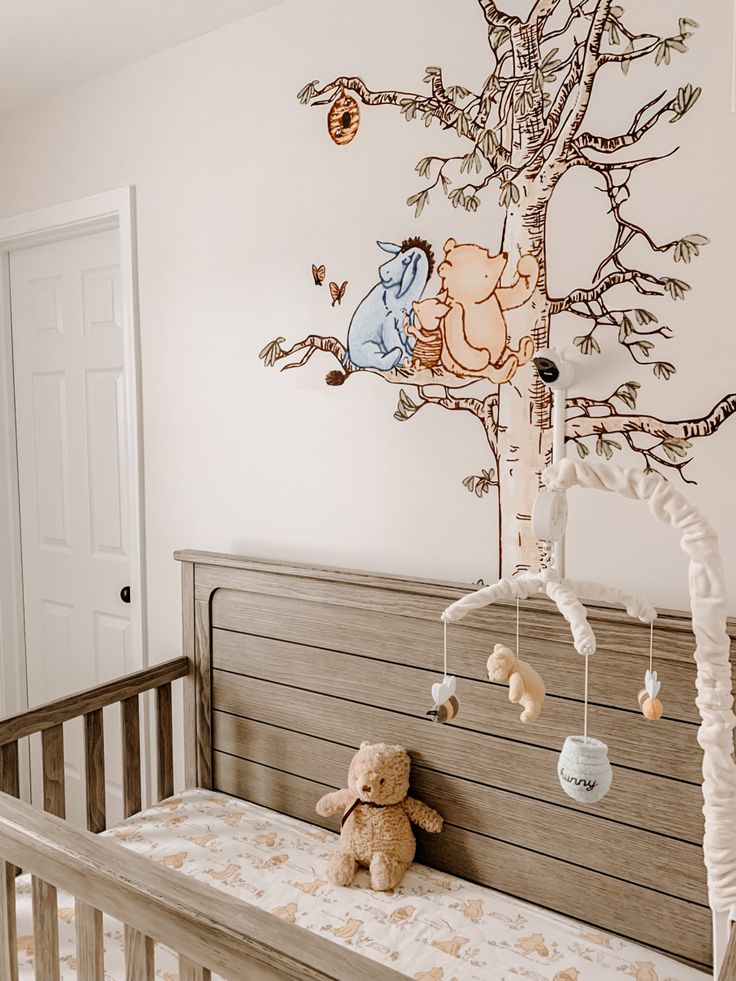 a baby crib with a teddy bear in it and a tree painted on the wall