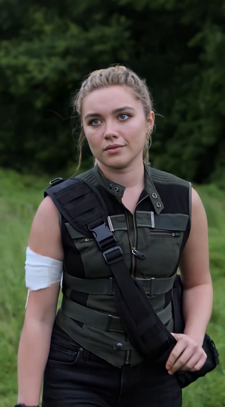 a woman in black vest and white shirt holding an arm cast on her left shoulder