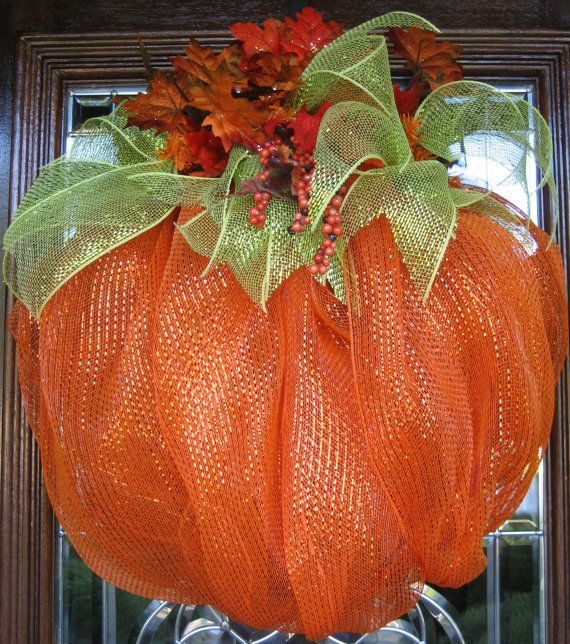 an orange mesh pumpkin with leaves and berries hanging from it's front door frame