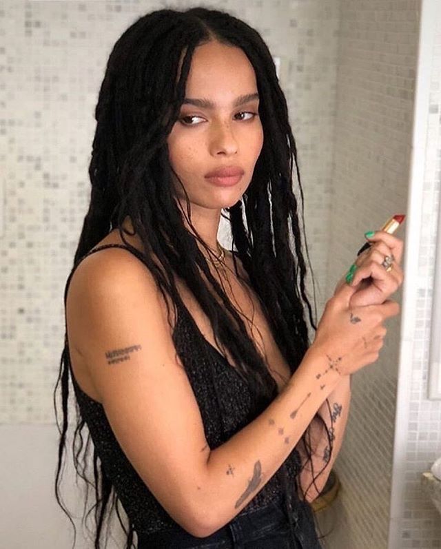 a woman with dreadlocks is brushing her teeth in the bathroom while holding a toothbrush