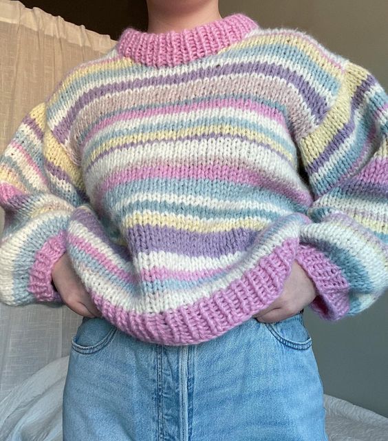 a woman standing in front of a bed with her hands on her hips wearing a colorful sweater