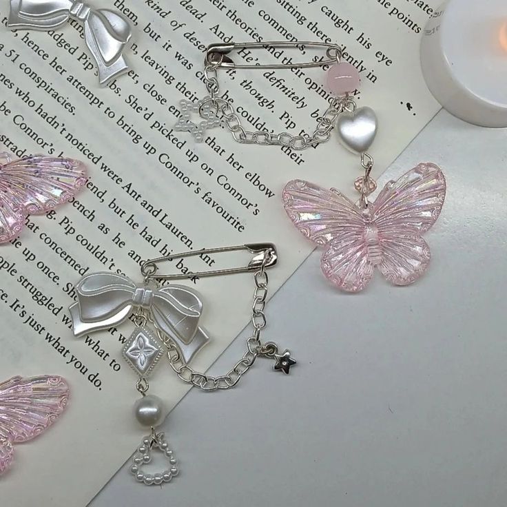 three butterfly shaped brooches sitting on top of an open book next to a candle