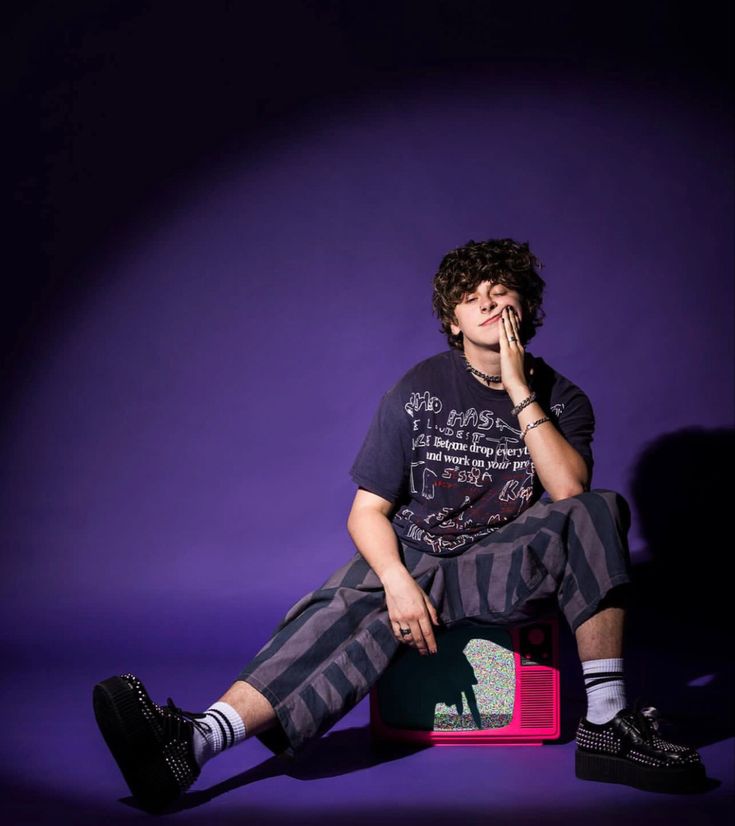 a young man sitting on top of a pink suitcase in front of a purple background