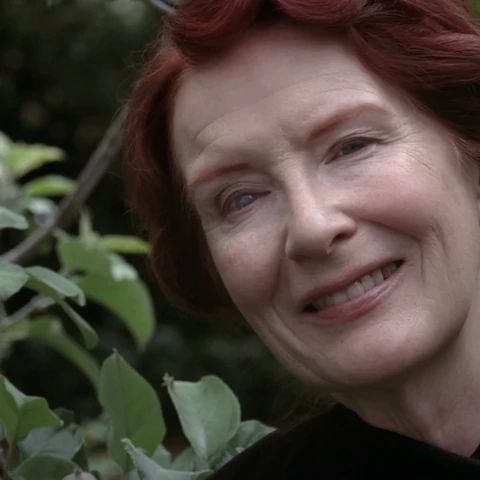 a woman with red hair is smiling for the camera while standing in front of some leaves